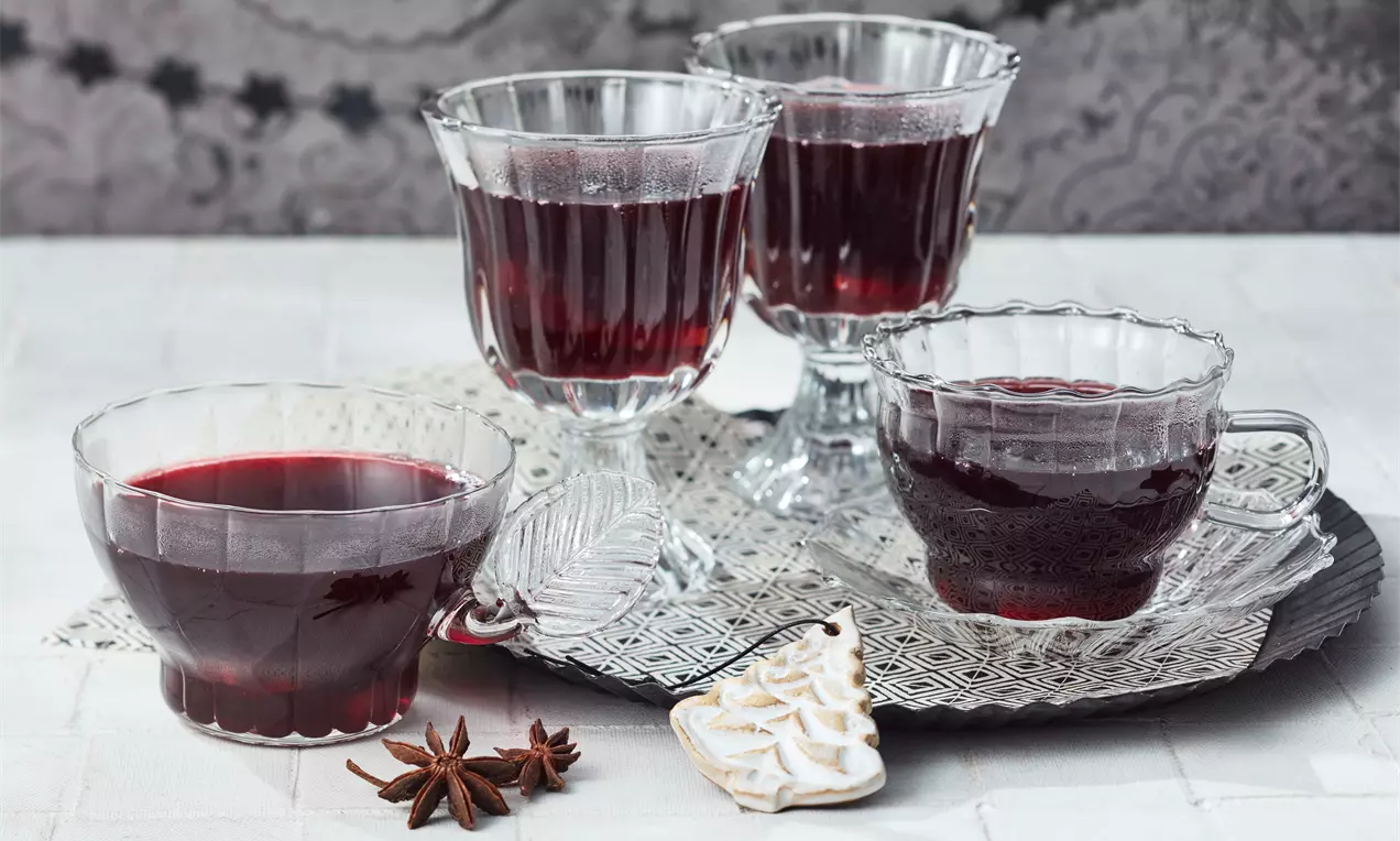 Glühwein in klarem hitzebeständigem Glas, tiefrot und dampfend, mit Orangenscheibe, Zimtstange und Sternanis, auf rustikalem Holztisch