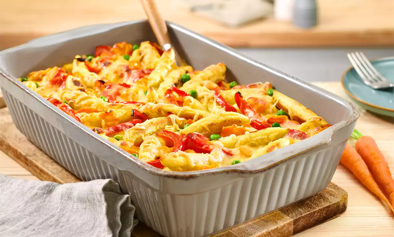 Schupfnudeln mit goldgelber Kruste, rotem Paprika und grünen Kräutern in einer rechteckigen Auflaufform auf einem Holzbrett