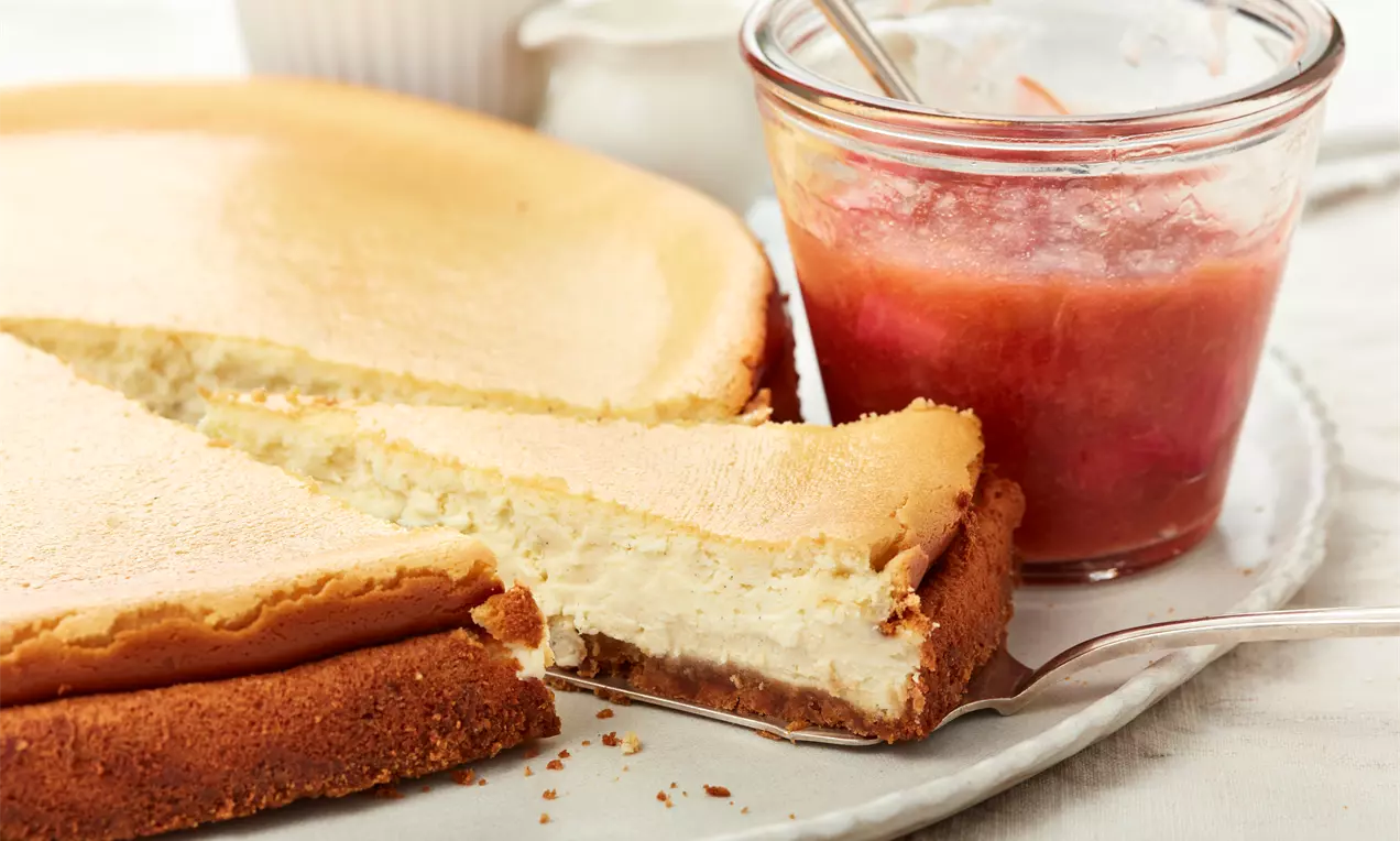 Käsekuchen mit Frischkäse auf Keksboden, cremig hellgelbe Füllung, leicht gebräunter Rand, mit frischen Beeren und Minzblatt garniert