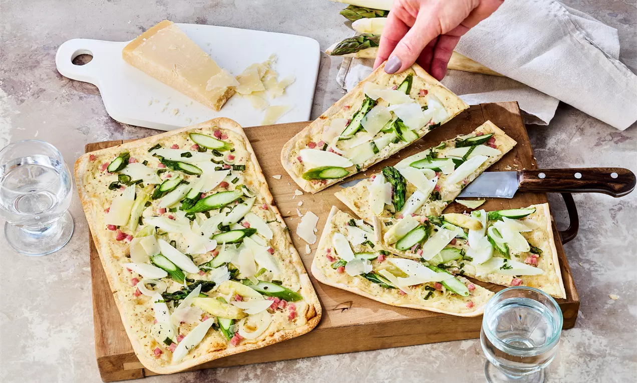 Knuspriger Flammkuchen mit grünem Spargel, Schinkenspeck, Lauchzwiebeln und Crème fraîche auf goldbraunem Boden – frisch aus dem Ofen serviert.