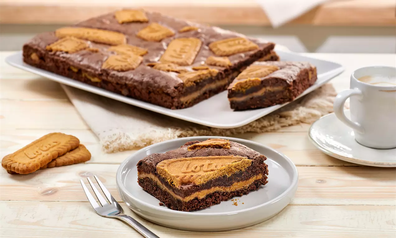 Kuchenplatte und Teller mit Lotus Brownie und Kuchengabel - saftige Schokoladen-Brownies mit einer Lotus Biscoff® Creme-Schicht und knusprigem Karamellgebäck obendrauf. einfaches Rezept