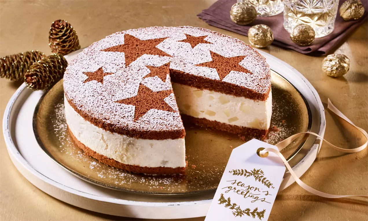 Runde Winter-Käse-Sahne-Torte mit braunen Teigböden, Sternen aus Kakaopulver und weißem Puderzucker auf goldfarbenem Teller