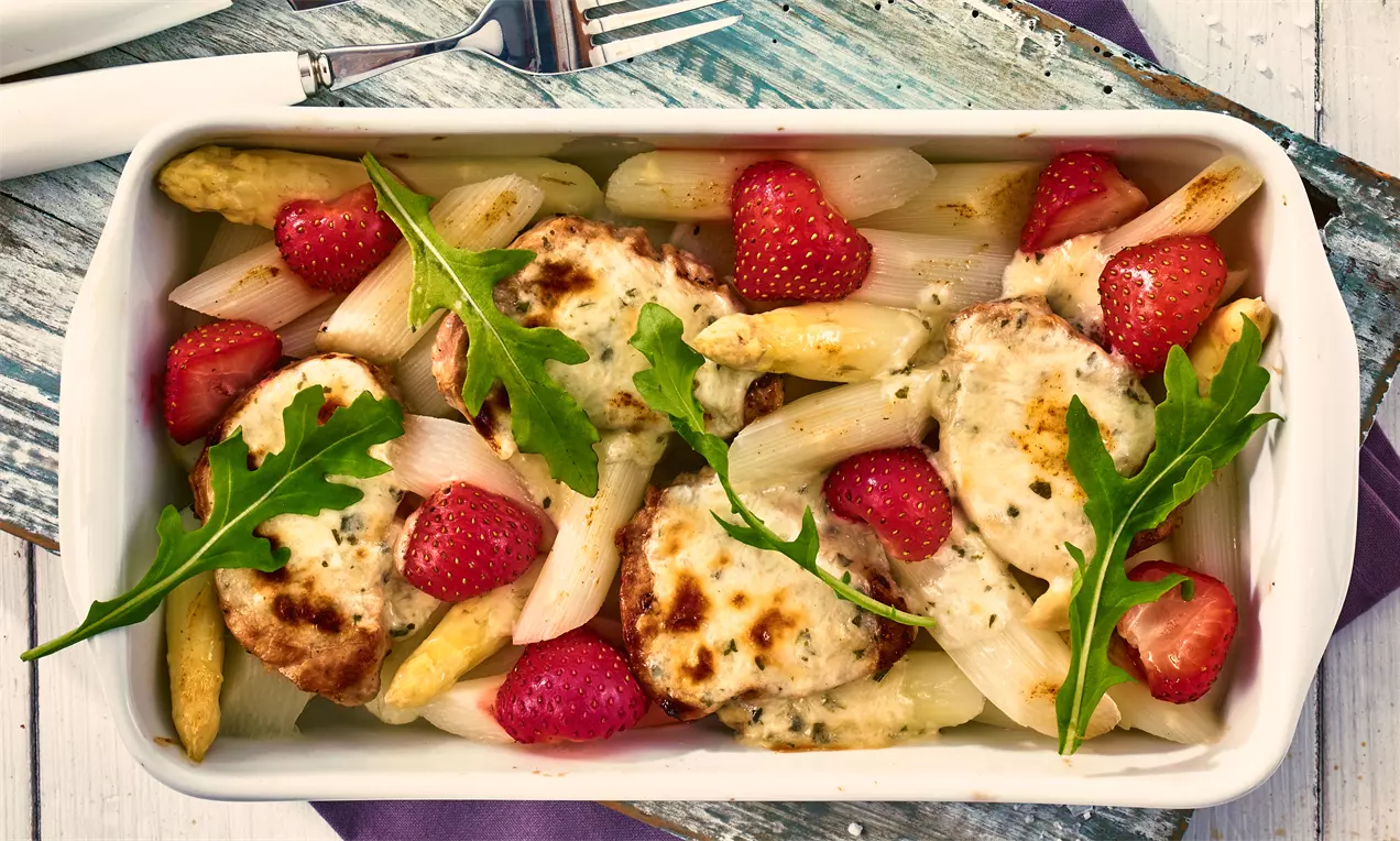 Weißer Spargel und rosa Erdbeeren mit goldbraun überbackenem Filet, garniert mit frischem grünem Rucola in einer weißen Keramikform