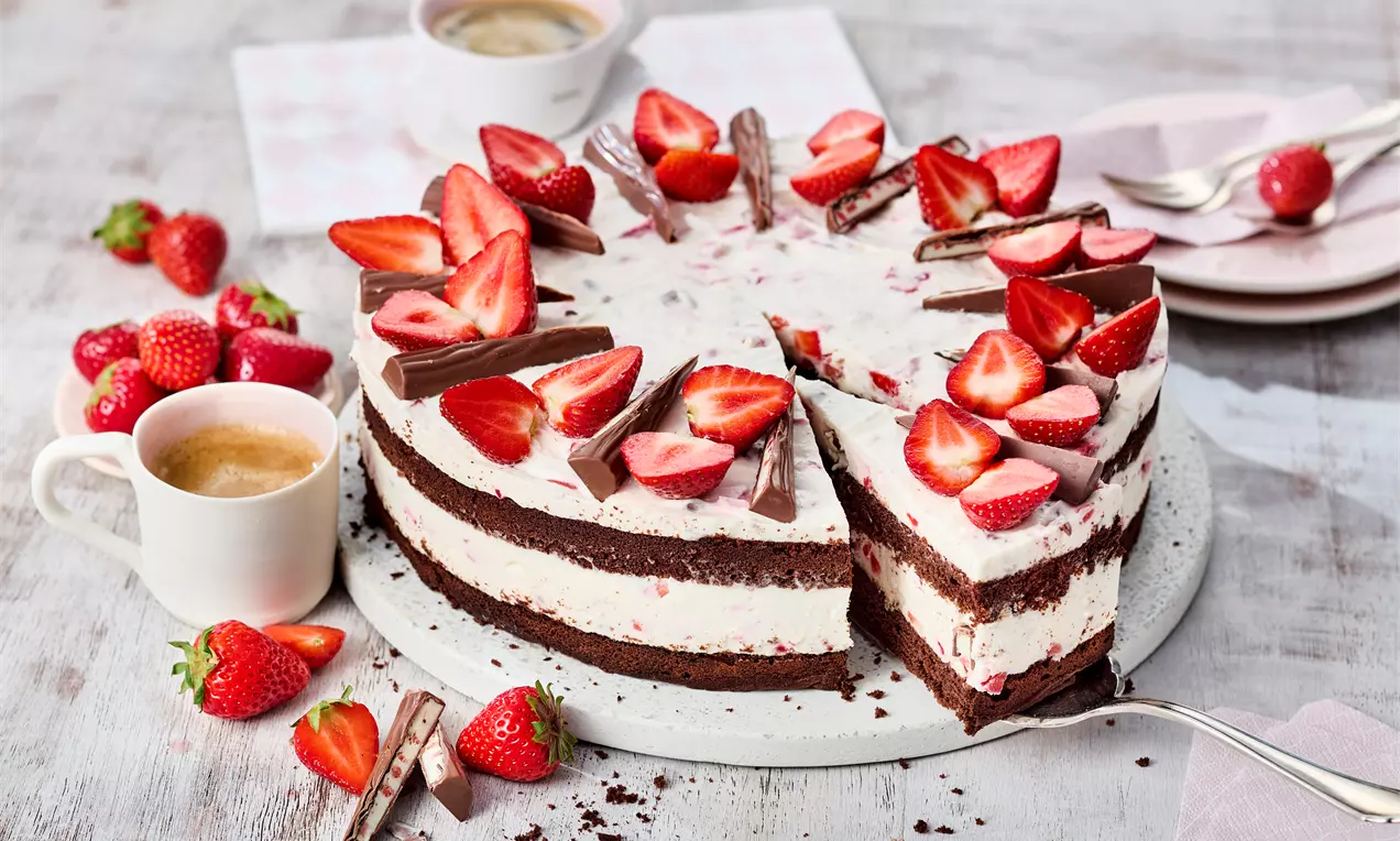 Eine runde Erdbeertorte mit dunklem Schokoladenboden, heller Sahnecreme und frischen Erdbeerstücken, angerichtet auf einem weißen Teller
