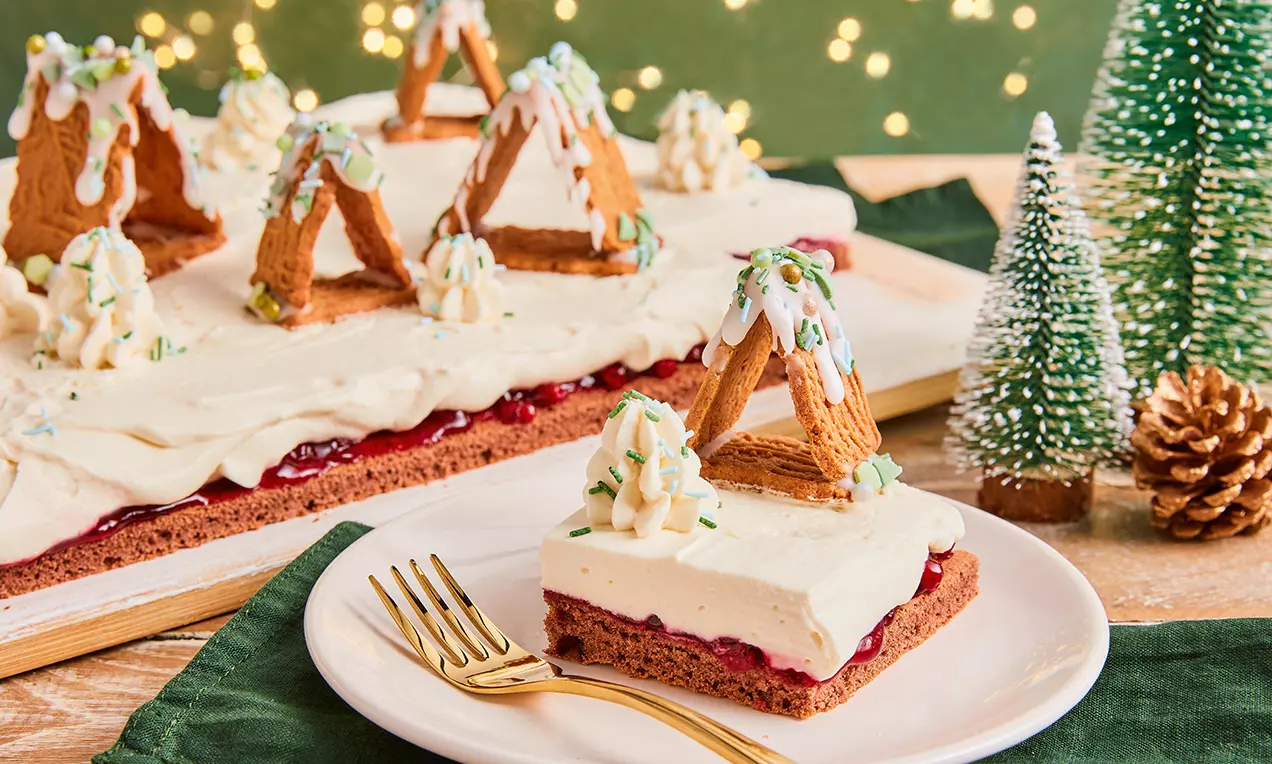 Weihnachtlicher Kuchen mit rotbraunem Boden, weißer Creme und Spekulatiushäuschen, dekoriert mit Zuckerguss und Pistaziensplittern