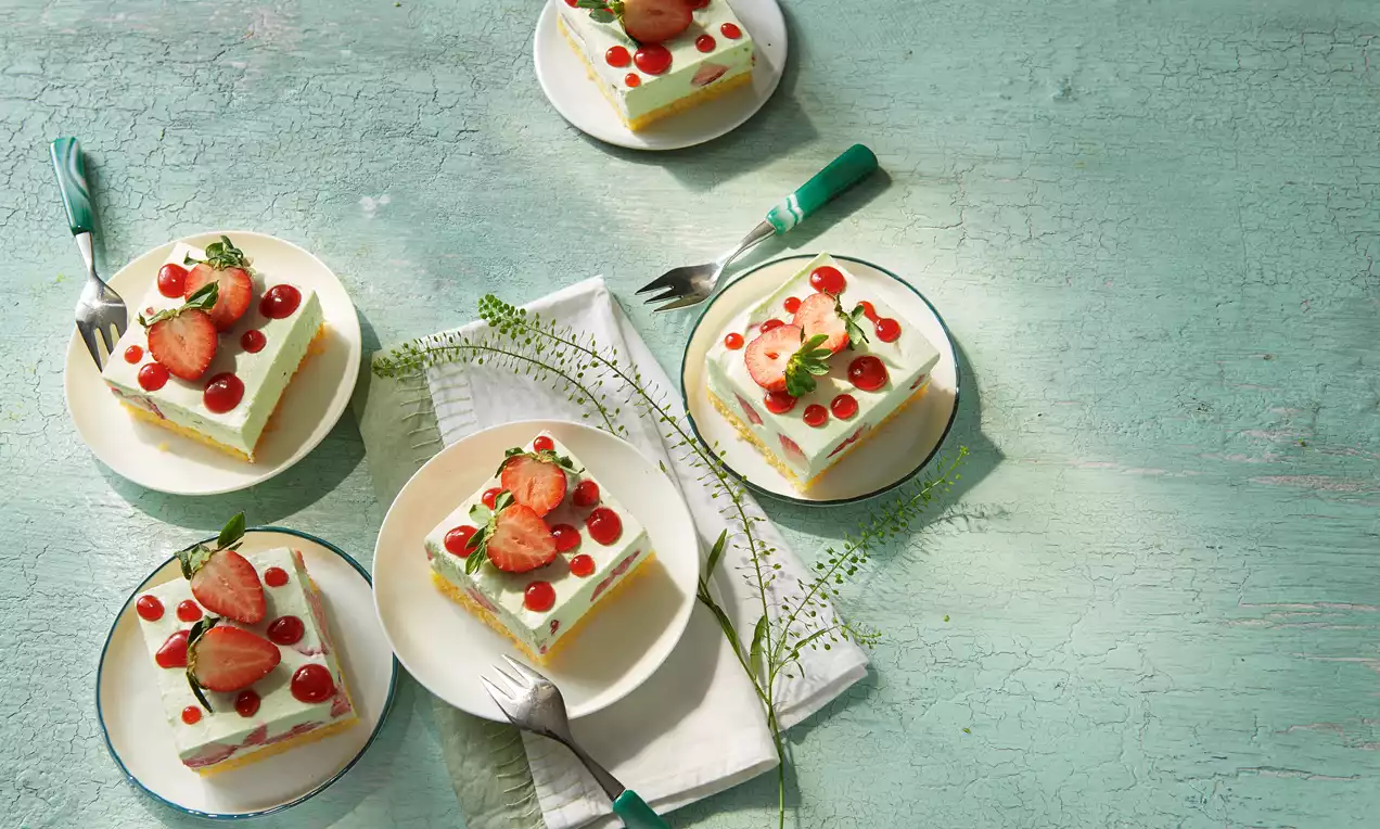 Waldmeisterkuchen mit saftigem goldbraunem Boden, pastellgrüner Waldmeister-Quark-Sahne und zahlreichen leuchtend roten Erdbeeren angerichtet