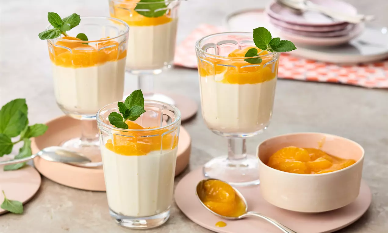 Cremige Quarkspeise in gläsernen Dessertschalen, getoppt mit orangefarbenem Fruchtpüree und frischen Minzblättern, arrangiert auf rosa Tellern