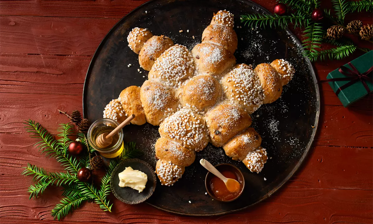 Weihnachtsstern aus goldenem Hefeteig, mit Puderzucker bestäubt, sichtbaren Mandelsplittern und Rosinen, auf Holzbrett angerichtet