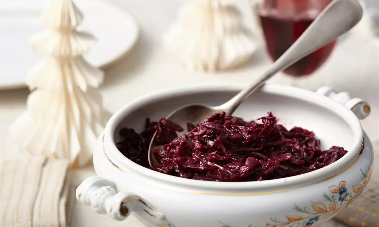 Dunkelvioletter Rotkohl mit glänzender, zart-weicher Textur in einer weißen, floral verzierten Porzellanschale mit silbernem Löffel