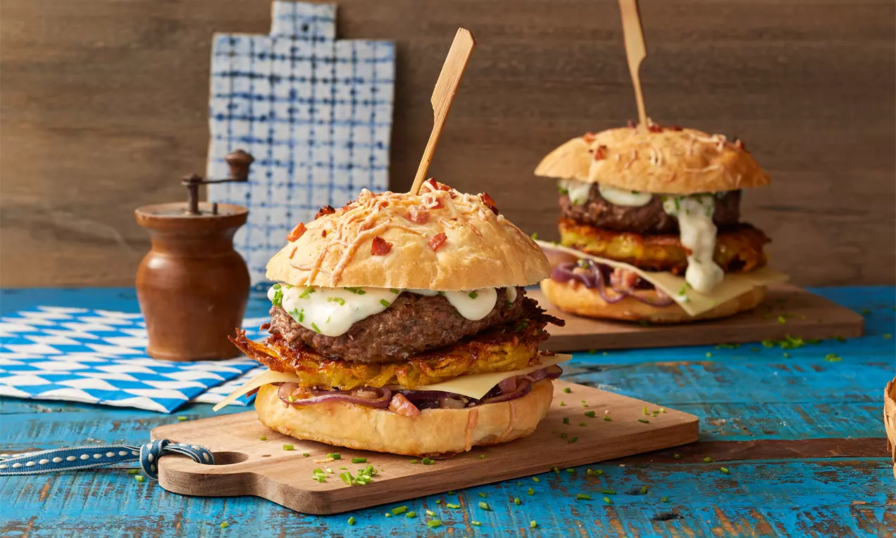 Rösti-Burger mit knusprigem Kartoffelrösti, saftigem Patty, Käse, Salat und Soße zwischen golden gebackenem Brötchen auf Holzbrett serviert