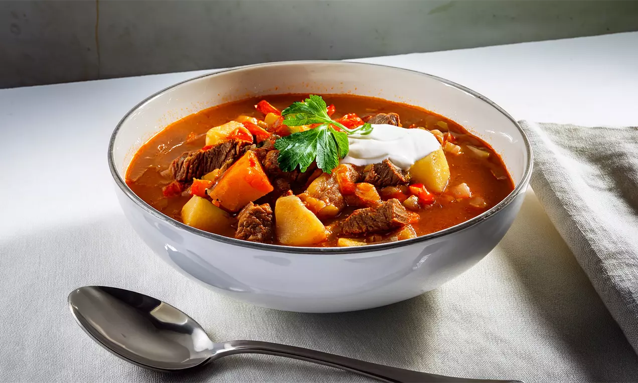 Suppenschale mit herzhafter Gulaschsuppe, frischen Kräutern und Creme fraîche - einfaches Rezept mit Gemüsestücken und Rindfleisch. Koche den Klassiker für perfekten Genuss!, AI-labeled image