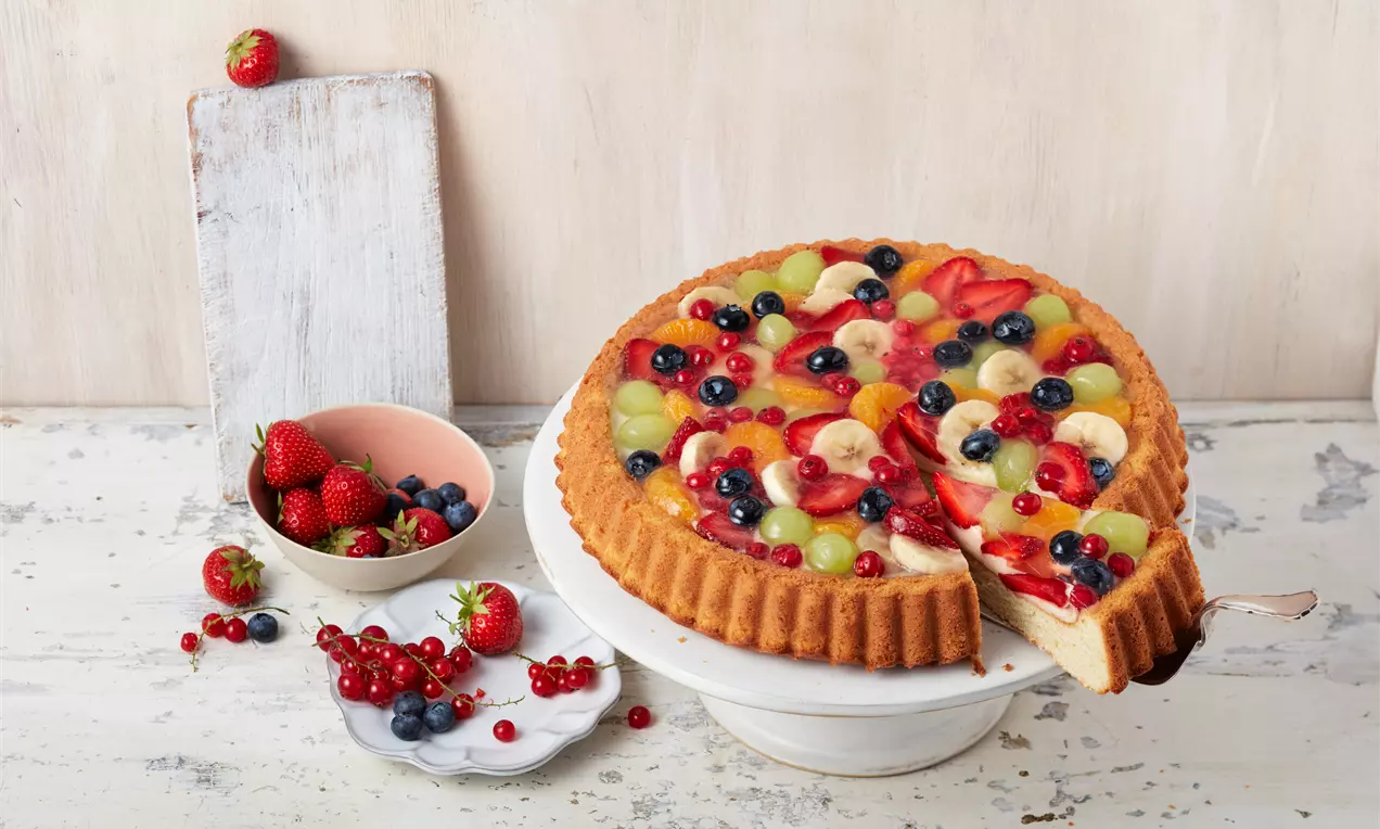 Obstkuchen mit Pudding saftige rote Erdbeeren, grüne Kiwischeiben und blaue Heidelbeeren auf glänzender Puddingcreme in goldbraunem Mürbeteig