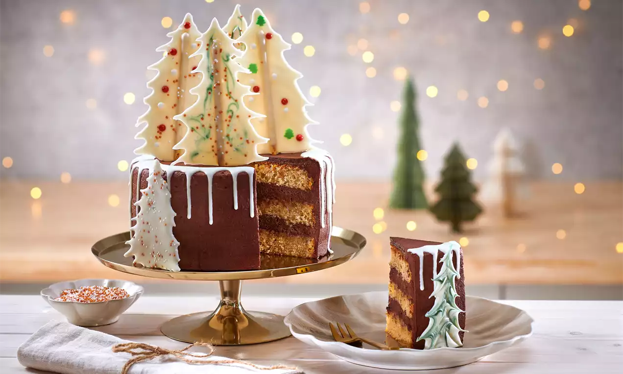 Weihnachtstorte mit schokoladenbrauner Ummantelung, weißer Zuckerglasur und dekorativen Schokoladentannen auf einer goldenen Tortenplatte