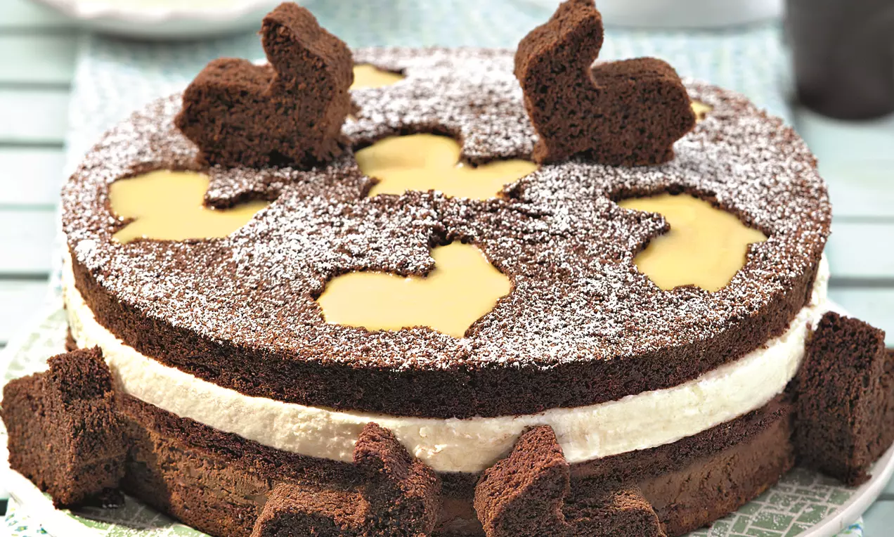 Schoko-Torte mit dunkelbrauner, lockerer Böden, weißer Eierlikörsahne, gelben Füllungen und Hasenformen aus Schokoteig mit Puderzucker bestäubt