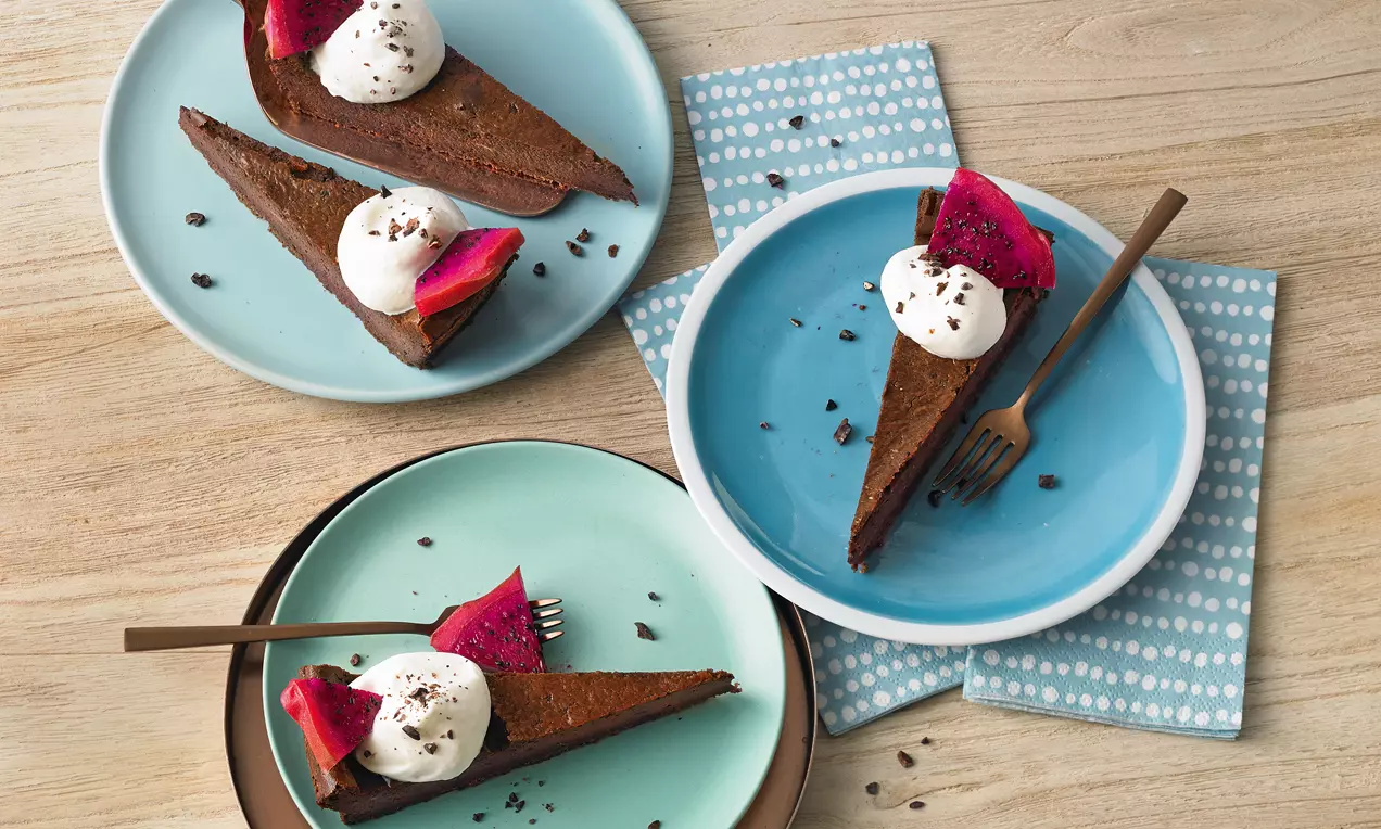 Dreieckige Stücke dunkler Schokoladen-Käsekuchen mit cremigem Sahnetupfen, Schokostreuseln und roter Blüte auf bunten Tellern angerichtet