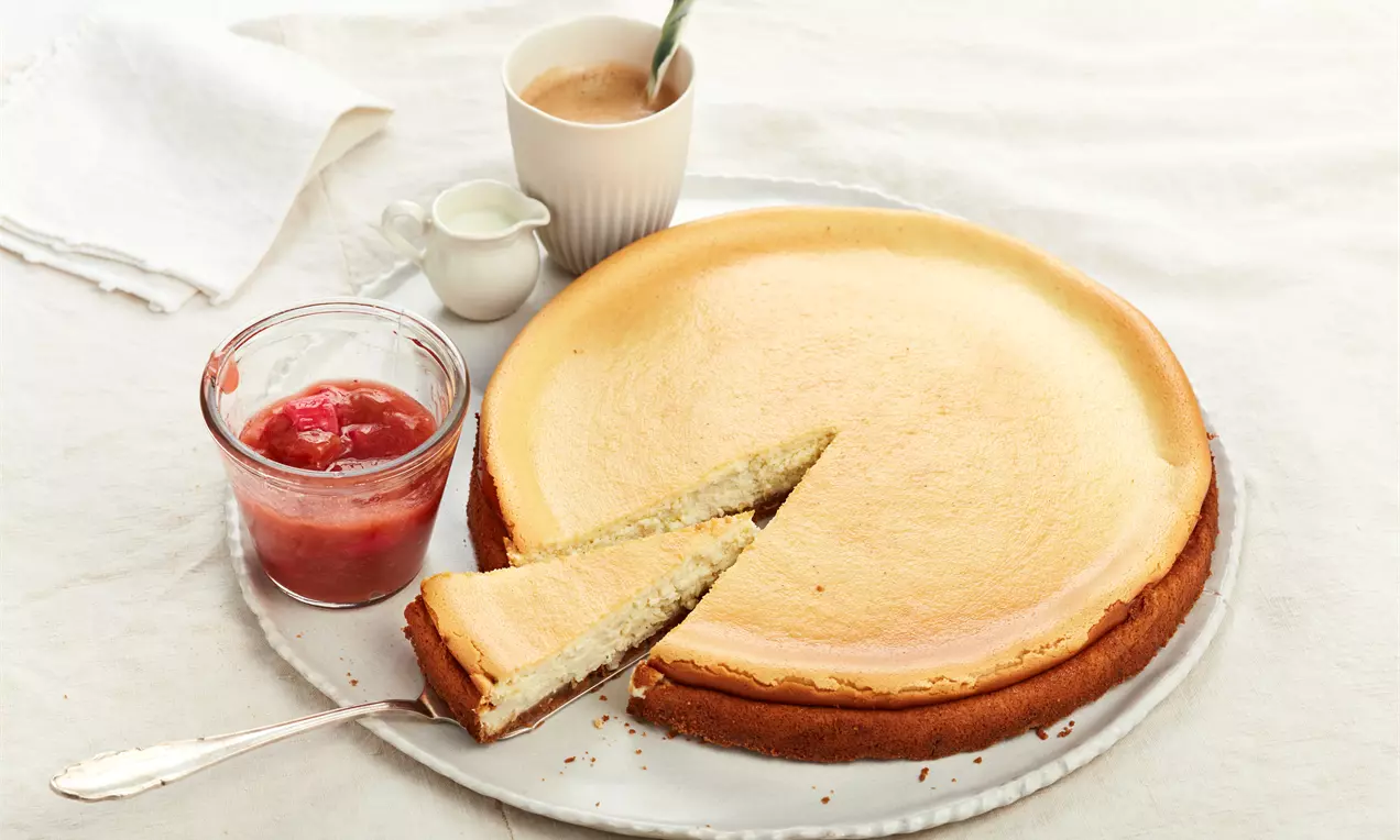 Käsekuchen mit Keksboden: goldbrauner Keksboden, cremige weiße Quarkfüllung, dünne Zitronenscheiben und Minzblatt als Garnitur