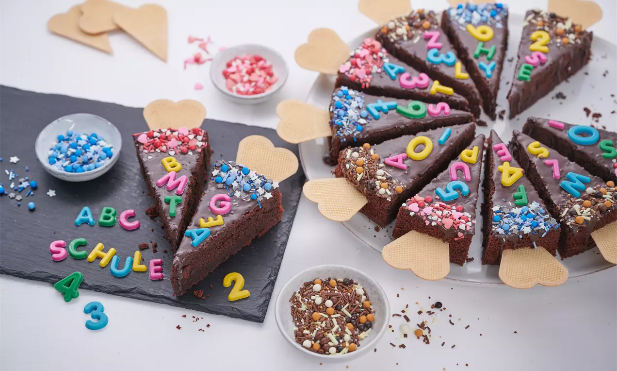 Dunkelbraune Kuchenschnitten mit bunter Zuckerdekoration und Waffelspitzen, auf einer weißen Platte und schwarzem Tablett angerichtet