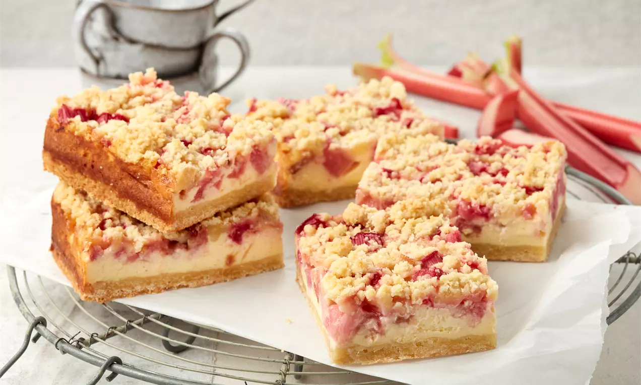 Rhabarber-Quarkkuchen mit goldbraunem Boden, cremiger Schicht und fruchtigen Rhabarberstücken, bedeckt von knusprigen Butterstreuseln auf Backpapier