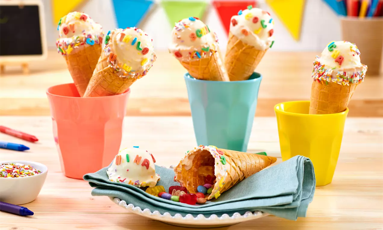 Eiswaffel-Schultüten mit Kuchenkugeln in Bonbonfarben, Zuckerguss, ABC-Buchstaben und Regenbogenstreuseln auf einem Teller