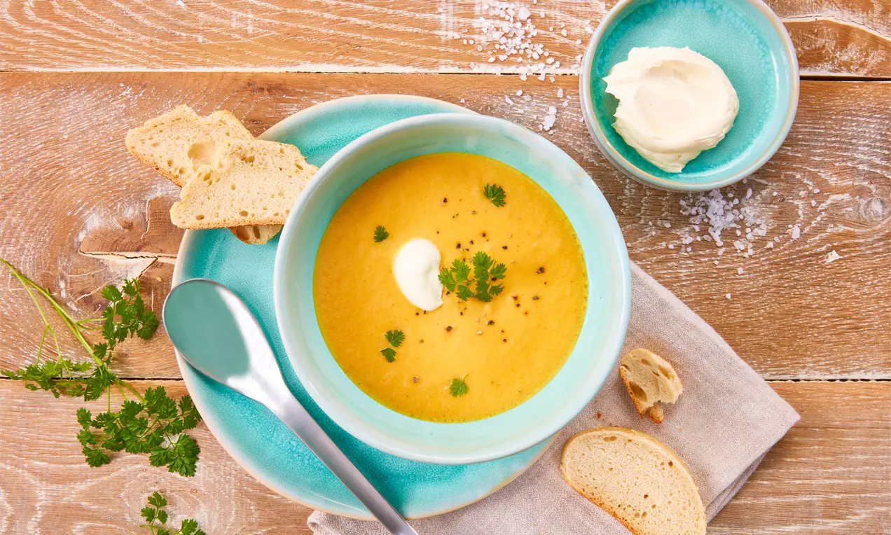 Möhrensuppe mit Kartoffelstücken, glatt orange-cremig, garniert mit frischer Petersilie und knusprigem Brot am Rand