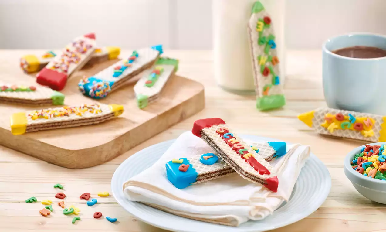 Waffel-Stifte aus goldbraunen Waffelröllchen, mit bunten Zuckerglasuren in Rot, Gelb, Grün und Blau verziert, stehend in einem Glas