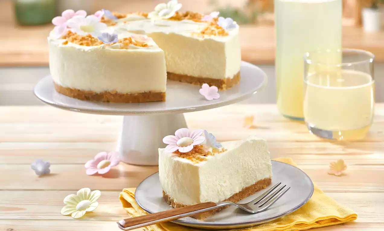 Zitronen-Quark-Kuchen auf braunem Keksboden mit cremiger Füllung, bestreut mit goldbraunen Streuseln, dekoriert mit bunten Blüten