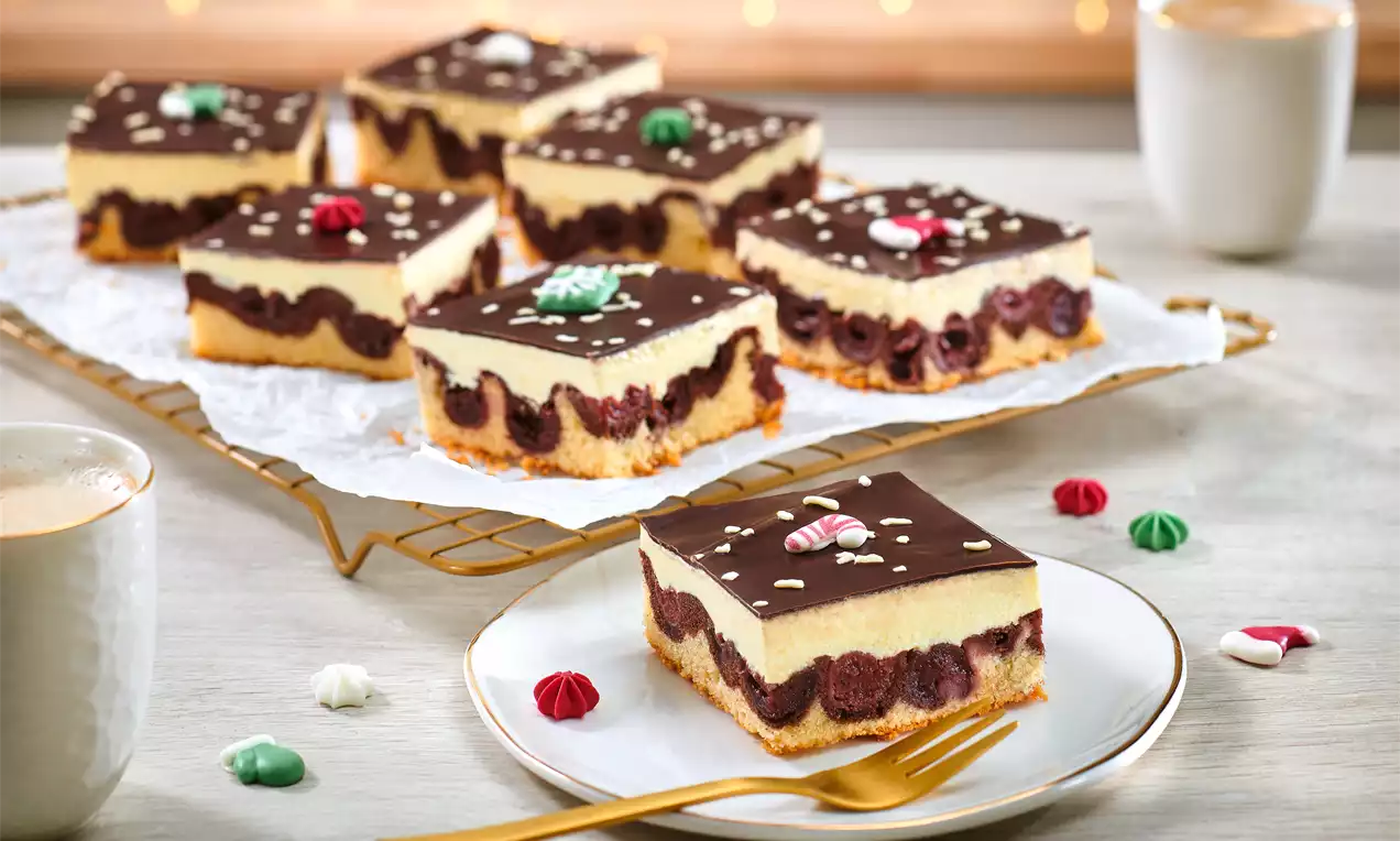 Donauwelle mit Schokoglasur, Vanillecreme und Kirschfüllung, dekoriert mit weihnachtlichen Zuckermotiven, auf einem Teller mit goldener Gabel