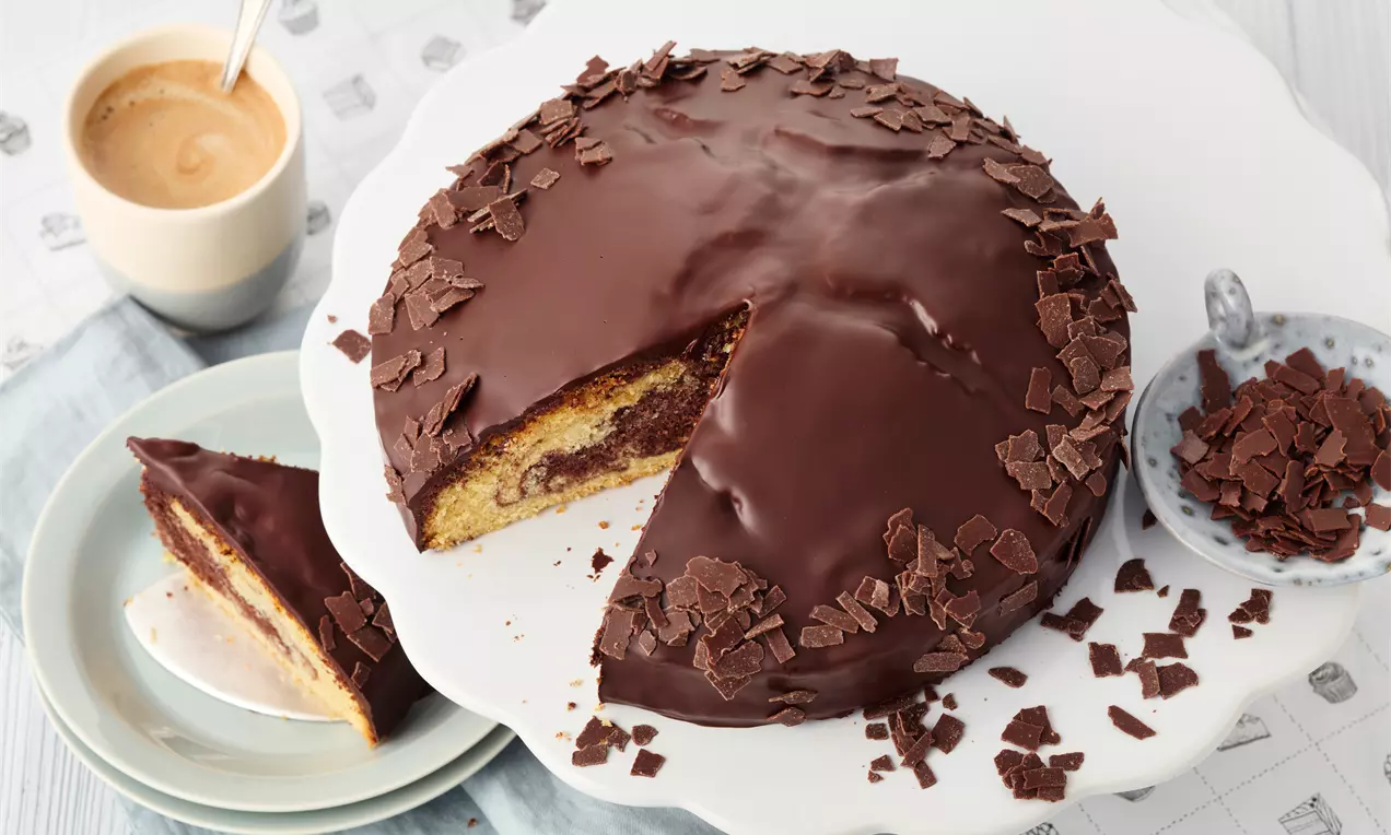 Kuchen mit goldbrauner Kruste und saftiger Innenstruktur, eine geschnittene Scheibe mit Puderzucker und roten Beeren auf hellem Teller