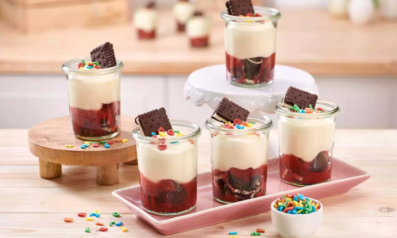 Einschulungs-Dessert im Glas mit weißer Schokoladen-Paradiescreme, Erdbeer-Himbeer-Grütze, Keksen und bunter Deko – perfekt für den besonderen Tag.