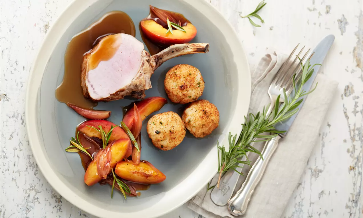 Saftiges Karree vom Duroc-Schwein mit rosa Kern, goldbraune Risottobällchen und glänzende Rosmarin-Nektarinen auf grauem Teller