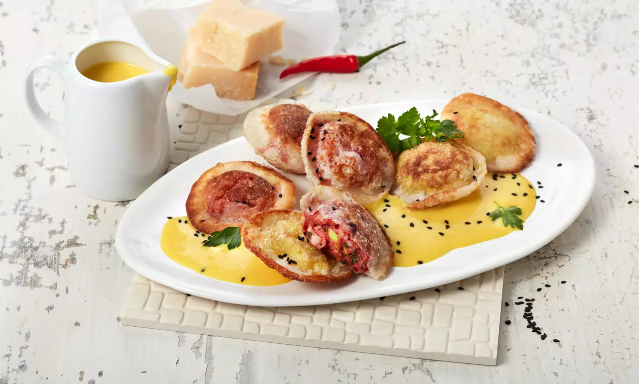 Gyoza-Ravioli mit goldbrauner Kruste auf gelber Sauce, mit Risottofüllung und Kräuterdekoration auf ovaler weißer Platte angerichtet