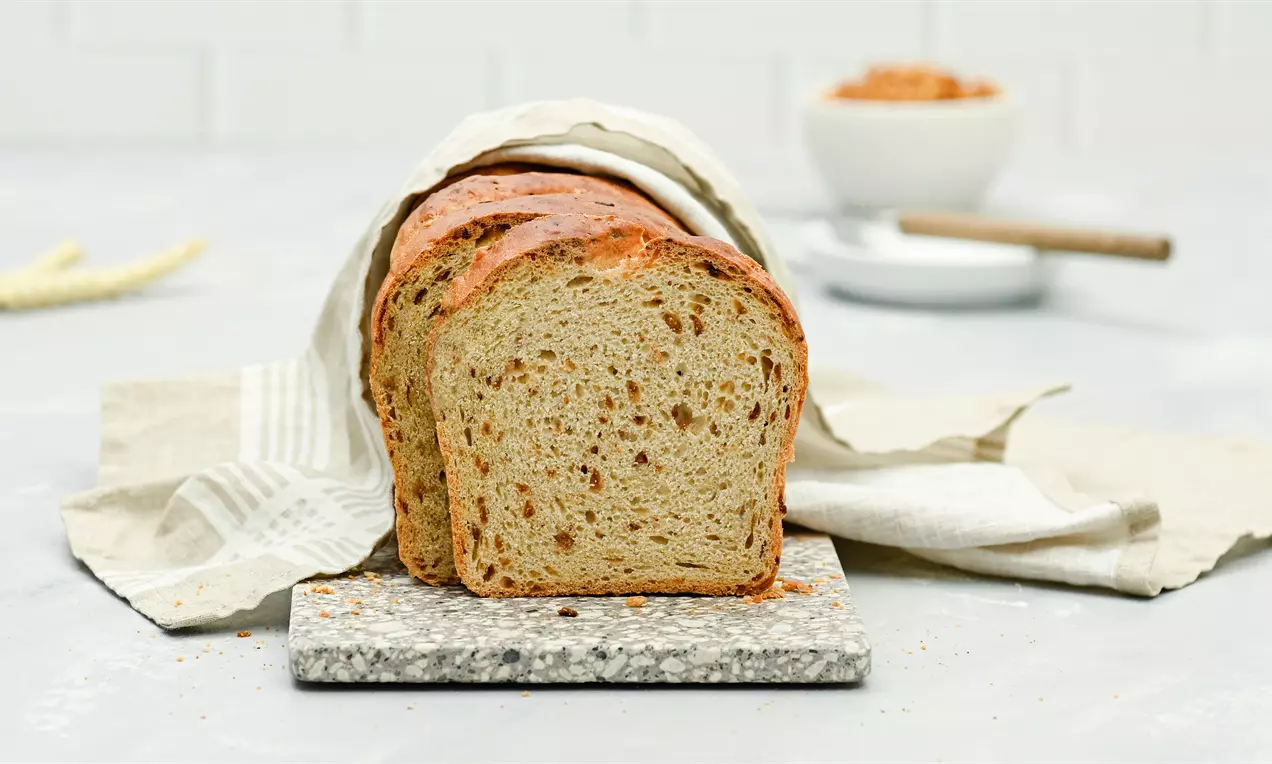 Aufgeschnittenes Zwiebelbrot mit goldbrauner Kruste und lockerer, leicht gesprenkelter Innenstruktur auf einem Steinbrett mit Stofftuch drapiert