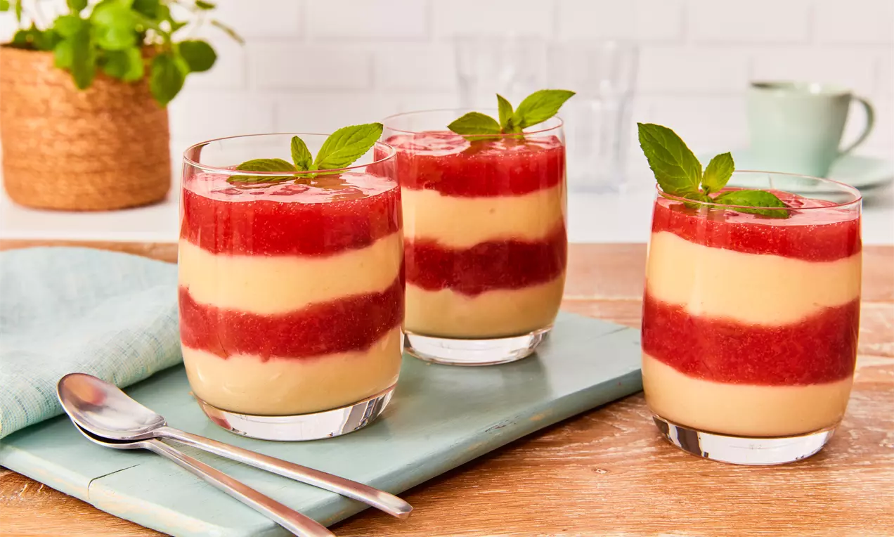 Veganer Grießbrei in Gläsern mit abwechselnden Schichten aus cremefarbenem Brei und roter Fruchtsoße, dekoriert mit frischen Minzblättern