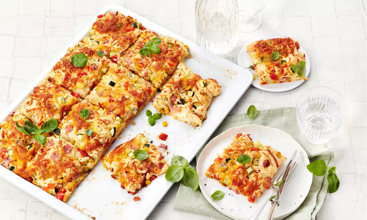 Schüttelpizza mit goldbrauner Kruste, geschmolzenem Käse, satter Tomatensauce, in Stücken mit frischem Basilikum auf Backblech
