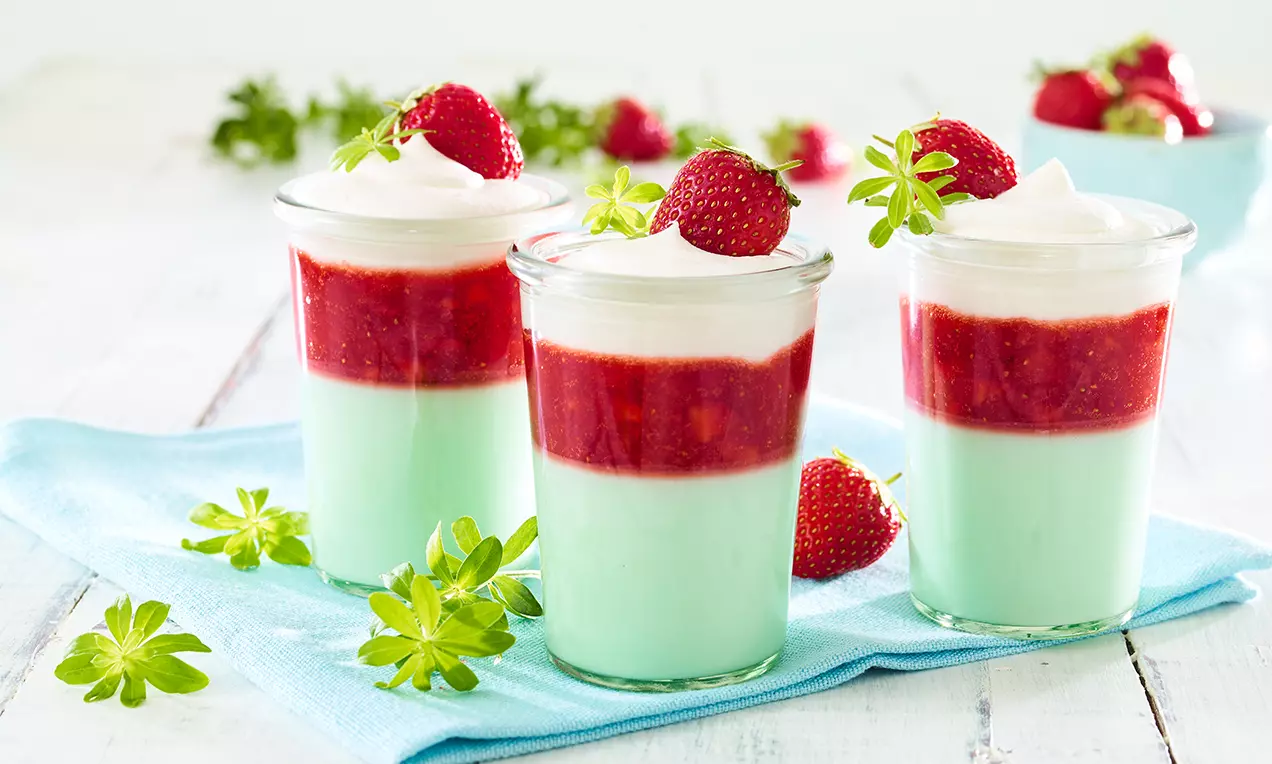 Schichtdessert in Gläsern mit mintgrüner Götterspeise, darauf leuchtend rote Erdbeerschicht, Sahnetupfen und frische Erdbeeren verziert