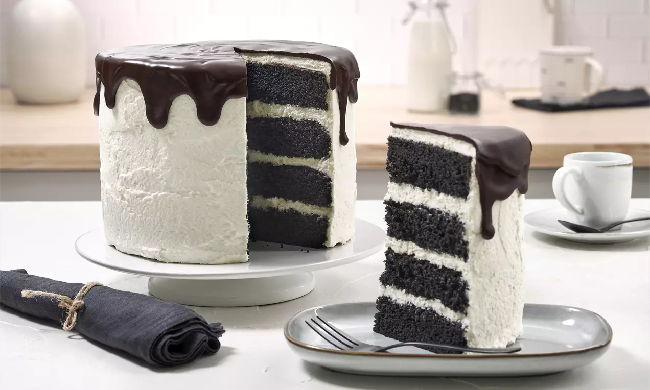 Schwarz-weiße Torte mit dunklen Schichten, weißem cremigen Überzug, Schokoladenglasur, ein Stück auf grauem Teller mit Gabel