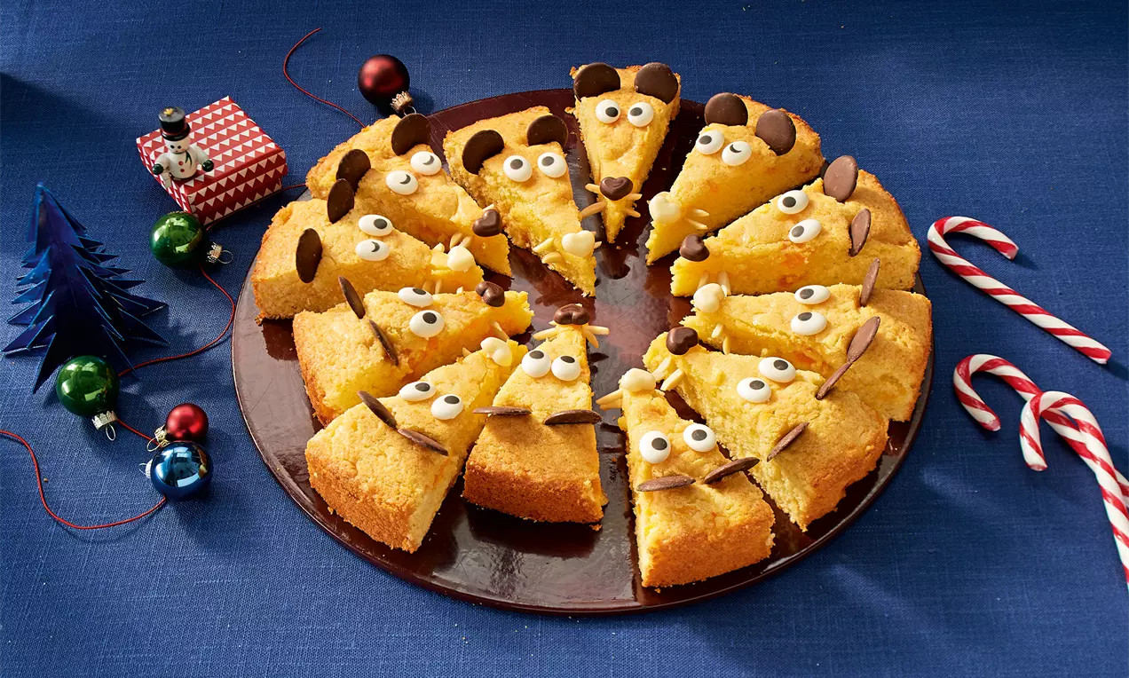 Kuchenstücke in Dreiecksform mit gelber Oberfläche, Augen aus weißen und braunen Süßigkeiten und Schokoladendekor auf brauner Platte