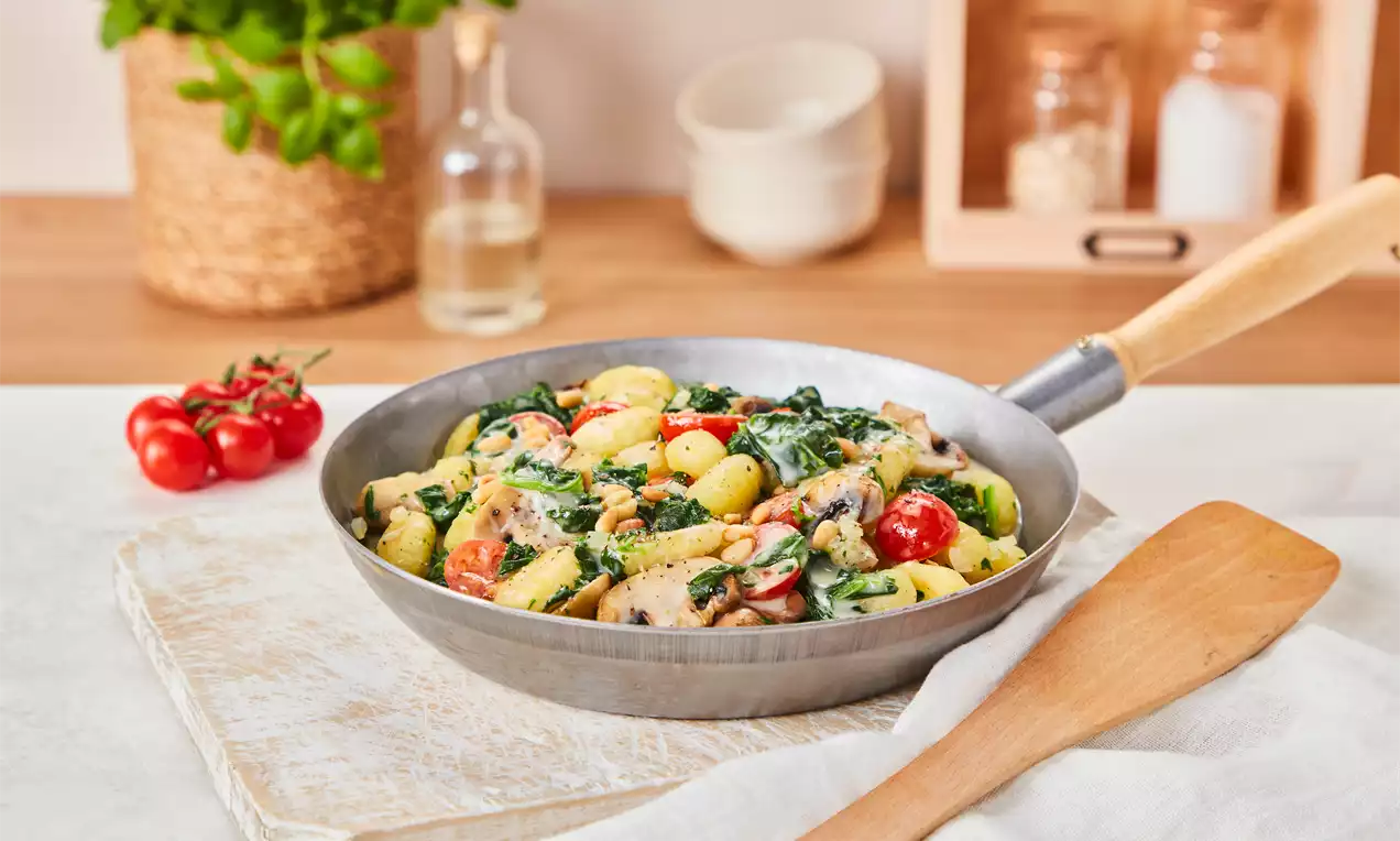 Vegane Gnocchi Pfanne mit goldbraunen Gnocchi, grünem Spinat, gebräunten Champignons und roten Tomaten, garniert mit Kräutern