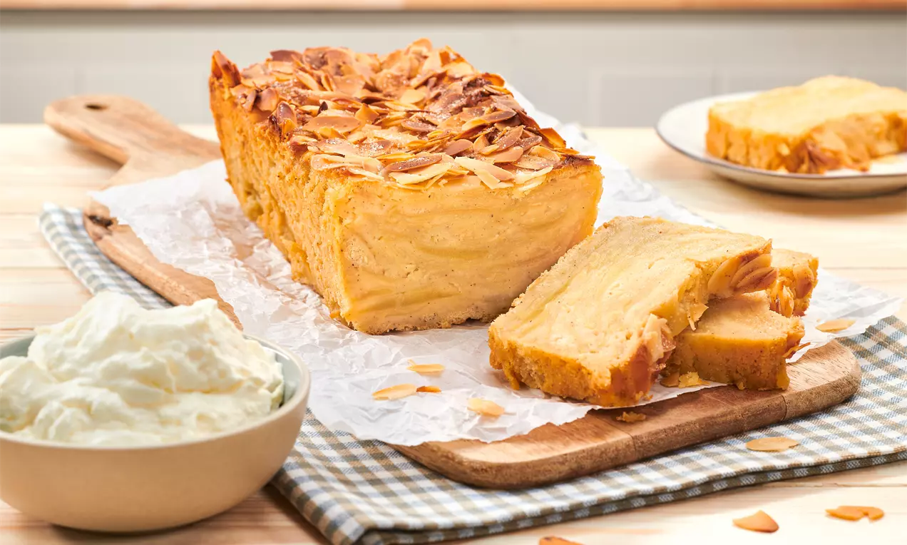 Unsichtbarer Apfelkuchen auf weißem Teller, goldbraune, karamellisierte Kruste und dünne Apfelscheiben sichtbar, mit Puderzucker bestäubt