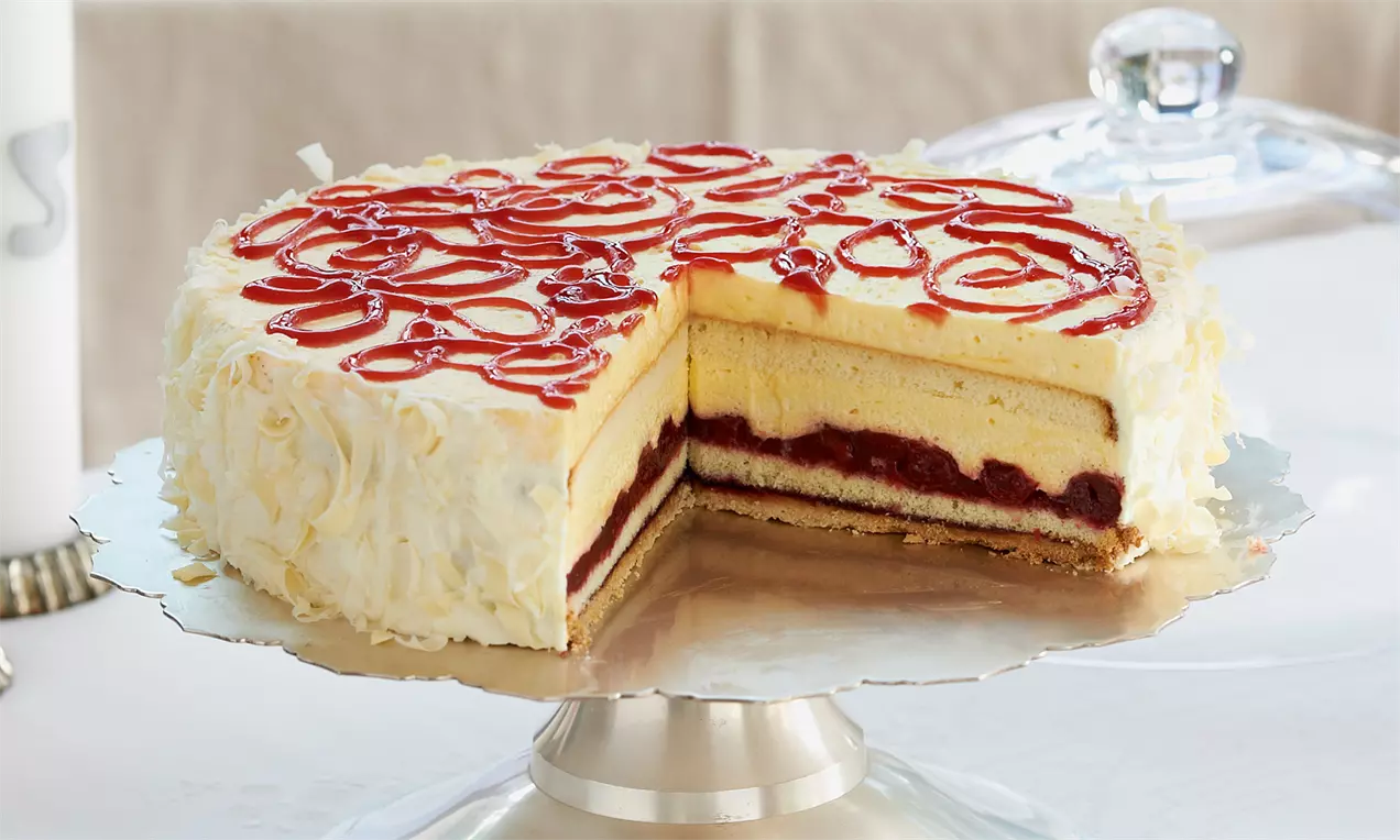 Himmel-und-Hölle-Torte mit gelber Cremefüllung, roter Fruchtmasse, weißer Schokoraspel-Verzierung und rotem Muster auf silberner Tortenplatte