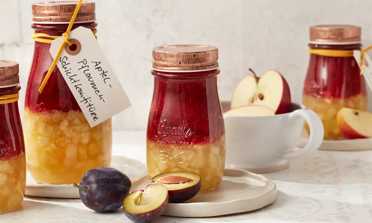 Apfel-Pflaumen-Schichtkonfitüre in Gläsern mit bronzefarbenen Deckeln, gelber Obstschicht, satter roter Fruchtschicht und beigefarbenem Anhänger