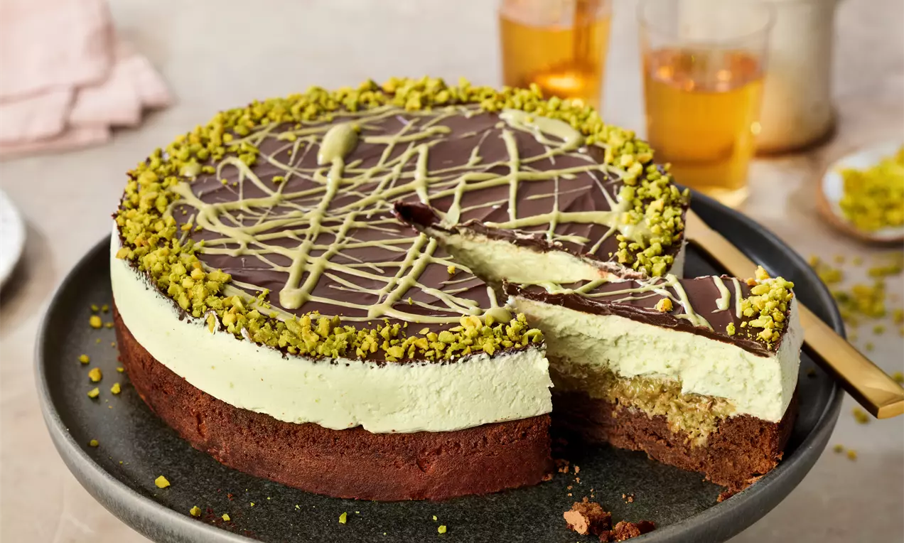 Dubai-Torte mit hellgrüner Pistaziencreme, knusprigem goldbraunem Kadayif, Pistazienstreuseln und einem angeschnittenen Stück auf einem Teller