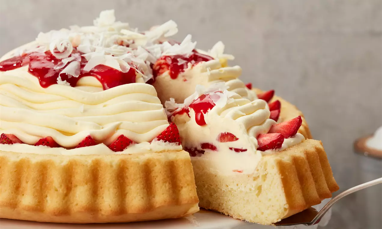 Spaghetti-Eis-Kuchen mit goldenem Mürbeteigboden, Sahnespiralen, Erdbeerhälften, roter Erdbeersoße und weißen Schokoraspeln auf Tortenplatte