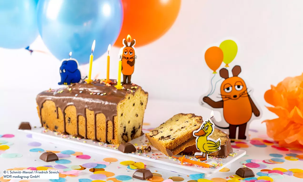 Schokokuchen in Kastenform mit Schokoladenguss, bunten Streuseln, Kerzen und Figuren der Maus umgeben von Luftballons auf weißem Teller