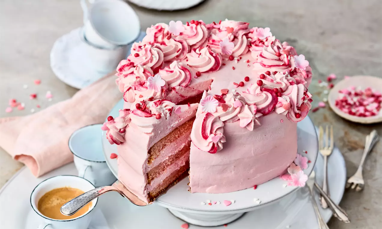 Rosa Torte mit saftigem Rührteig, cremiger heller Quark-Creme, frischen Himbeeren und zarten Zuckerstreuseln auf weißem Teller