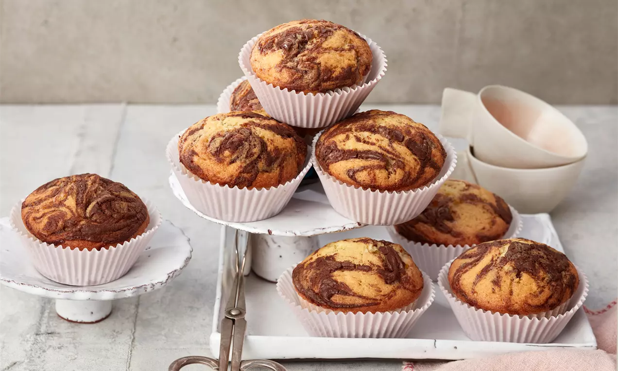 Nutella®-Muffins mit cremiger Nutella-Füllung, goldbrauner Oberfläche, Schokospänen und Papierförmchen auf hellem Teller