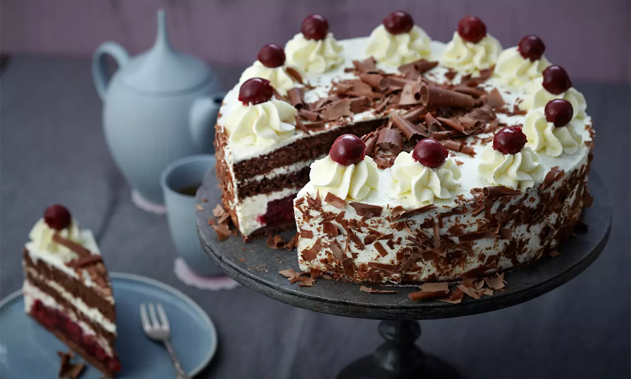 Schwarzwälder Kirschtorte mit dunklen Schokoladenböden, weißen Sahnehauben, glühenden Kirschen, Schokoraspeln und einer Kirsche obenauf