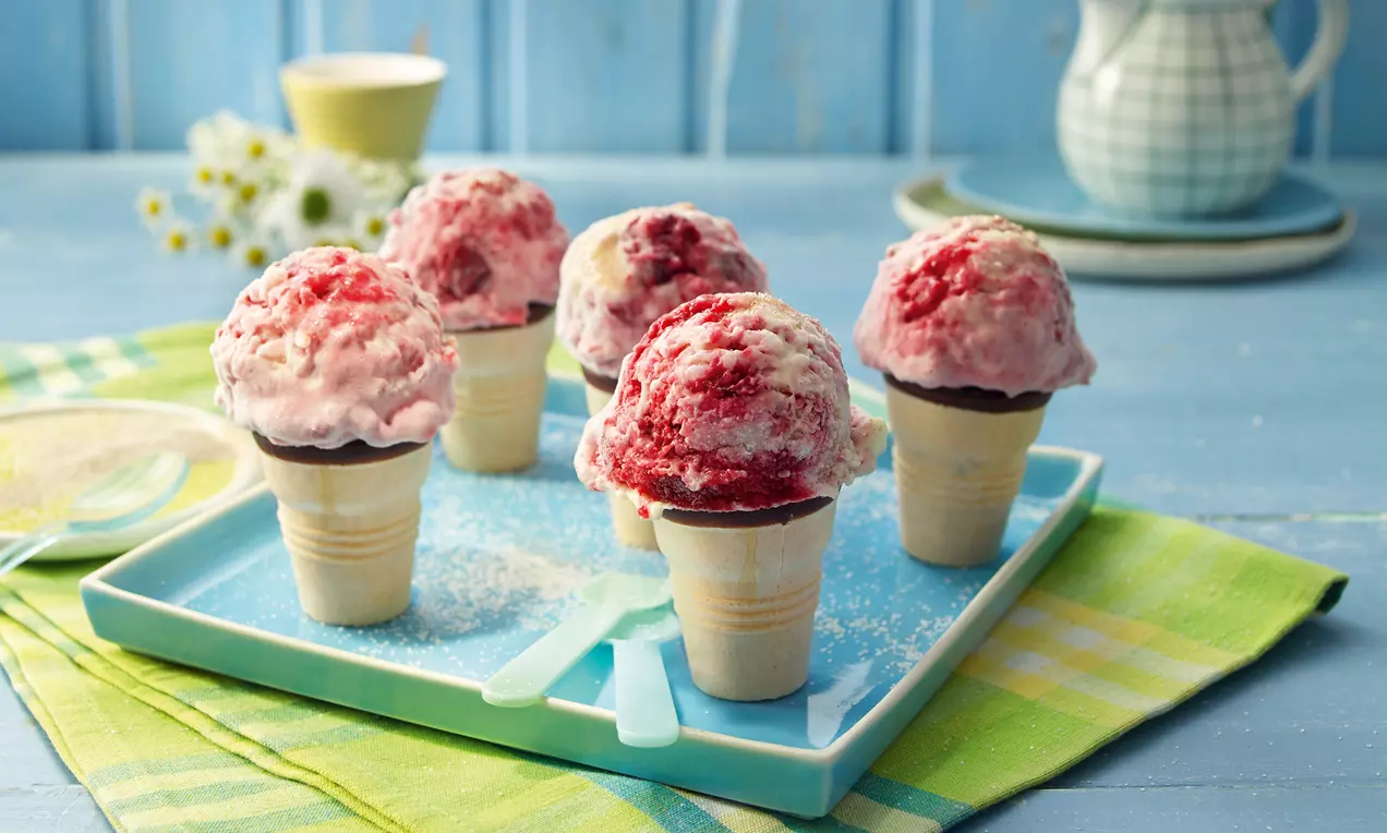 Milchreis Eis in einer klaren Glasschale, cremig weißer Milchreis mit leuchtend roter Grütze und einem Silberlöffel