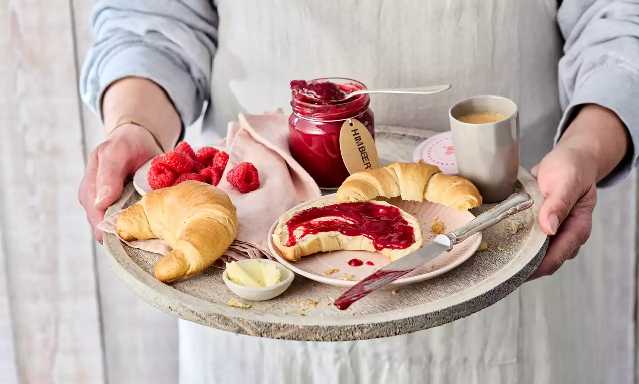 Himbeermarmelade ohne Kerne in Einmachglas, tiefrote Masse mit glänzendem Schimmer, daneben frische Himbeeren und Holzlöffel