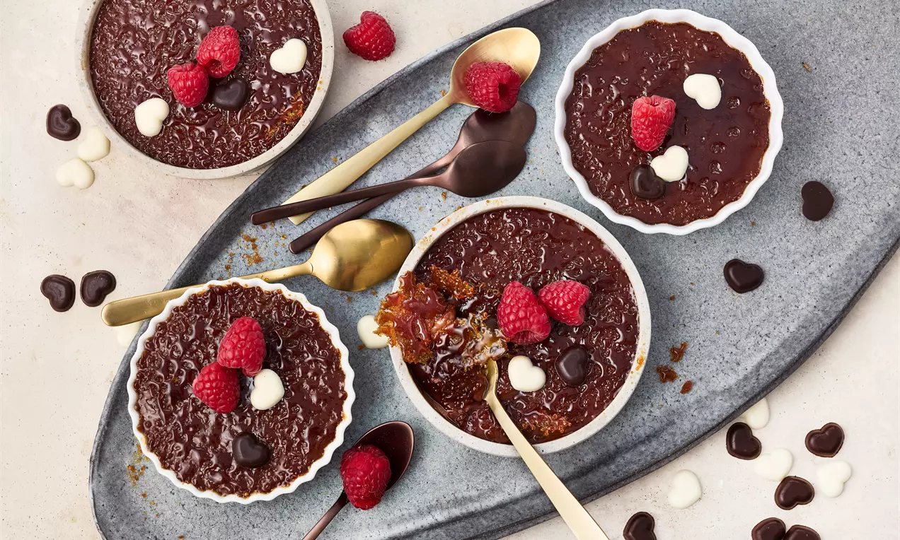Schoko Crème Brûlée mit Zartbitterschokolade und feinem Kakao, veredelt mit knuspriger Karamellschicht und frischen Himbeeren als fruchtiges Topping – ein elegantes Dessert für Schokoladenliebhaber.